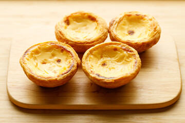 Stack of Portuguese sweet dessert egg tart or Pastel de Nata on wooden board on wooden table.  Selective focus.