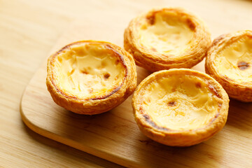 Stack of Portuguese sweet dessert egg tart or Pastel de Nata on wooden board on wooden table.  Selective focus.