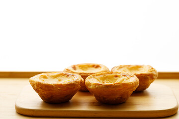 Stack of Portuguese sweet dessert egg tart or Pastel de Nata on wooden board on wooden table.  Selective focus.