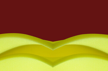 sheet of thin yellow sponge foam material on dark red background. creative foam with copy space