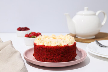 Red velvet cake on pink plate, towel, teapot and berries on white background