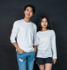 Fototapeta premium Asian Couple in Matching White Shirts Striking a Pose with Dark Background