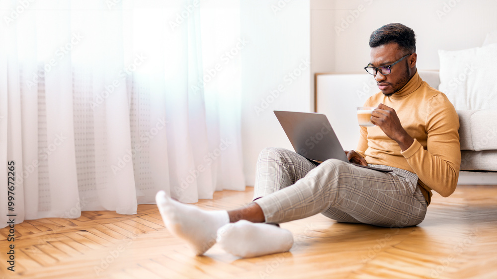 Poster Freelance Career. Serious Black Freelancer Guy Working On Laptop Computer And Having Coffee Sitting On Floor At Home. Selective Focus