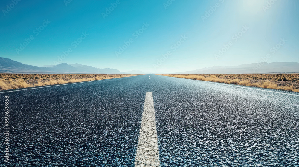 Wall mural wide asphalt highway stretches into clear blue horizon, surrounded by vast open land and distant mou