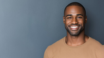Obraz premium A confident african american man with a bright smile stands against a gray wall, exuding positivity and approachability with a casual tan shirt and relaxed demeanor, copy space