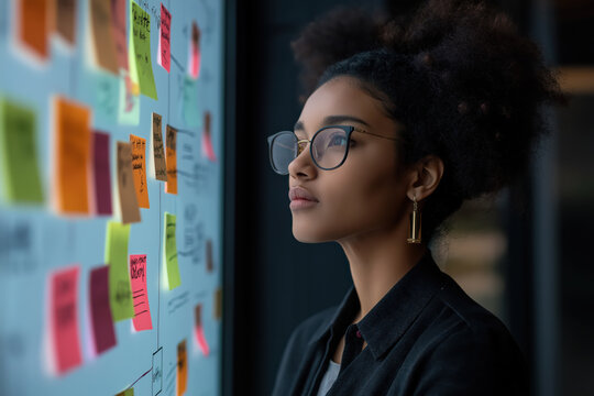 A woman wearing glasses looks at a board with colorful sticky notes