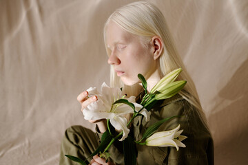 Side view medium closeup studio shot of young woman with albinism holding fresh white lily flowers