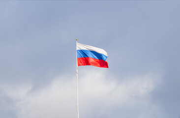 Russian tricolor flag waving in the wind against a blue sky.