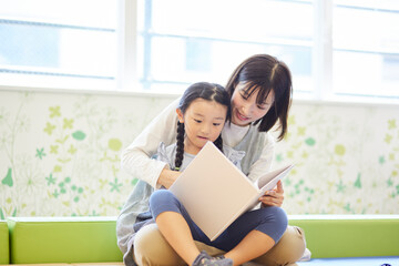 保育園で園児と絵本を見る女性の先生
