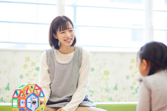 託児所でおもちゃで子供と遊ぶ保育士の女性