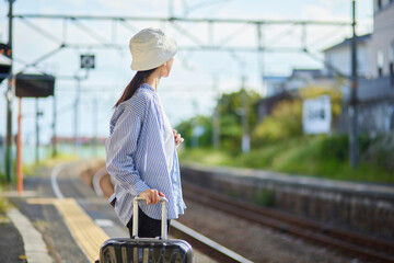 駅のホームで電車を待つ旅行中の日本人女性