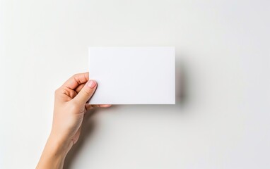 Fototapeta premium Hand holding a blank white card against a light background. Mockup template for greeting cards and invitations.