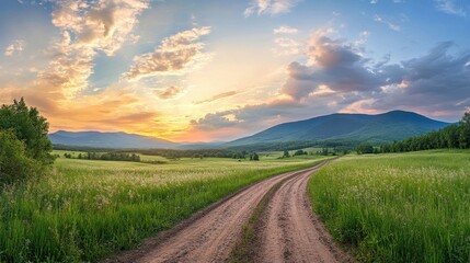 Fototapeta premium Winding Dirt Road Through Green Field and Mountains at Sunset