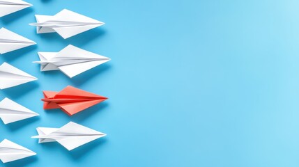 Fototapeta premium A single red paper airplane stands out from a line of white ones on a light blue background.