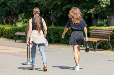 Two women walking down a sidewalk, one of them carrying a purse