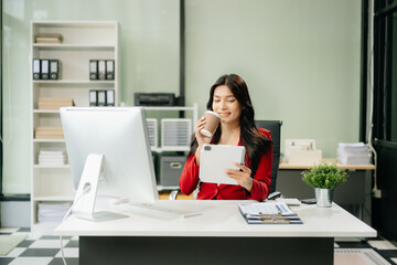 Obraz premium Asian woman using laptop and tablet while sitting at her working place
