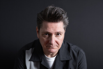 Fototapeta premium Close-up portrait of a very serious and sad 50-year-old man looking at camera. Dark background. Copy space. Concept of sadness, depression and mental health