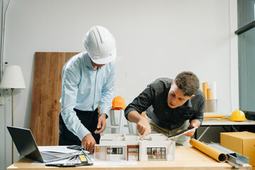 Professional collaboration in architecture. Two engineers work on construction plans, using tools like laptops, tablets, and scale models.