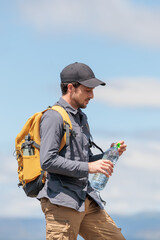 Naklejka premium Young man enjoying nature. Drinking water is very important and healthy. Always stay hydrated. Hiking in the mountains, observing the landscape. Practicing sports and physical activity. Moments