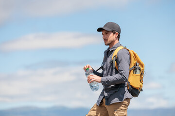 Naklejka premium Young man enjoying nature. Drinking water is very important and healthy. Always stay hydrated. Hiking in the mountains, observing the landscape. Practicing sports and physical activity. Moments