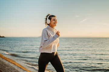 Young caucasian woman running or jogging on the beach at sunset