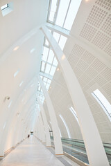 Naklejka premium Airport, corridor and architecture in tunnel with pillar, design and empty walkway from low angle with skylight. Hallway, beams and wall in atrium with conveyor belt for luggage, transport and travel
