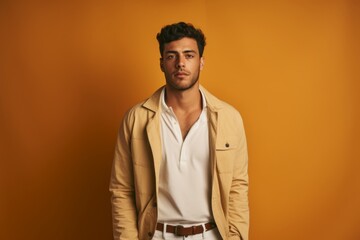 Fototapeta premium A man in a tan jacket and white shirt stands in front of a yellow wall