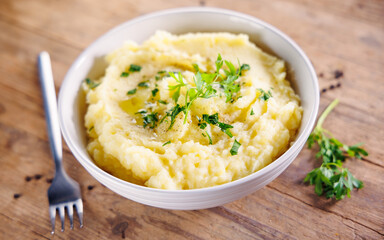 Bowl of mashed potatoes with butter and parsley on wooden background. Perfect for comfort food and homemade meal visuals