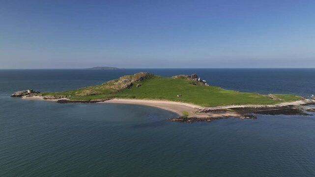 Ireland's Eye, County Dublin, Ireland, May 2023. Drone slowly pulls backwards showcasing the picturesque beach on a bright sunny day with Lambay Island in the distance.