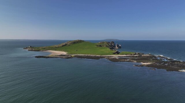 Ireland's Eye, County Dublin, Ireland, May 2023. Drone orbits clockwise around the picturesque Isle on a sunny afternoon showcasing the Beach and Martello Tower with Lambay Island on the horizon.