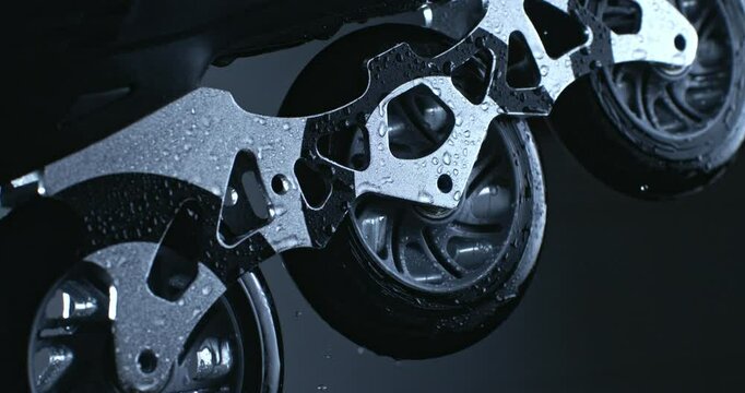 Super slow motion close up of wet inline roller sports skates wheels being rotating with energetic movement with splashing water drops by master isolated on dark background at 1000 fps.