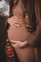 pregnant woman in wollen beige stylish coat and scarf outdoor in the forest walking. Vintage toned noise image no face