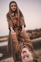 A pregnant woman and her daughter walk through an autumn forest, along the beach near the river in stylish beige coats. Noise blurred toned vintage image