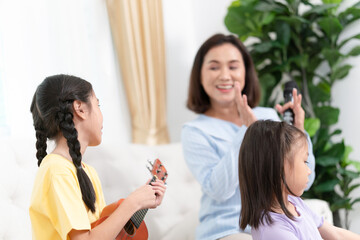 Cheerful mother and daughter relaxing together in living room, Asian mom enjoying with child while singing and playing the guitar in living room at home