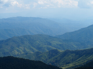 Mountain view against the sky. Aerial top view above green pass to rocky deep gorge with sharp sheer crags silhouettes against huge mountain under clouds in blue sky. 