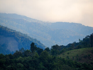 Mountain view against the sky. Aerial top view above green pass to rocky deep gorge with sharp sheer crags silhouettes against huge mountain under clouds in blue sky. 