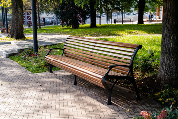 A sturdy wooden bench is elegantly positioned on a wellmaintained brick sidewalk in a lovely park, providing a perfect spot for relaxation and enjoyment of the beautiful surroundings