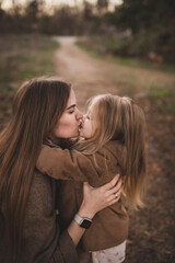 A pregnant woman and her daughter walk through an autumn forest, along the beach near the river in stylish beige coats. Noise blurred toned vintage image