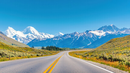 Scenic highway winding through lush green meadows with stunning snow-capped mountains under a clear blue sky