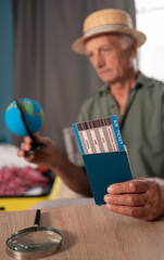 Male retiree preparing to travel and explore the world. Senior male sitting using smartphone to book for a hotel, for his retirement holiday.