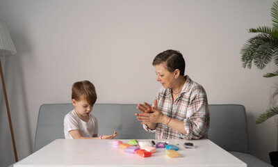 Smiling mother helps her small son to sculpt figurines from plasticine. Children's creativity