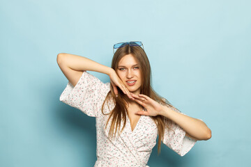 Naklejka premium Young woman in a light dress, sunglasses on a blue background in the studio.