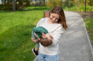 Caucasian woman holding her toddler son during walk in park. 