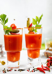 Bloody mary glasses with celery,olives,red hot pepper and cocktail spoon on light bar background.