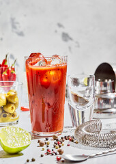 Luxury glass of pepper bloody mary with cocktail utensils and lime,olives and pepper on light board.