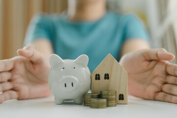 Person Protecting Piggy Bank, Stacked Coins, and Wooden House Model. Savings, Real Estate...