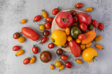 Mixed colorful ripe tomatoes top view on wooden board and scattered on grey stone table background.