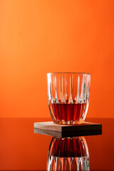 Glass of liquor scotch whiskey and ice cubes on warm orange background and reflective table top. Space for text