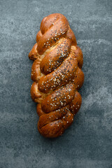 Homemade challah, traditional braided bread loaf with poppy and sesame seeds on a concrete...