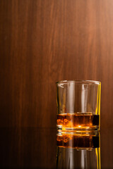 Glass of liquor scotch whiskey and ice cubes on wooden background and reflective table top. Space for text